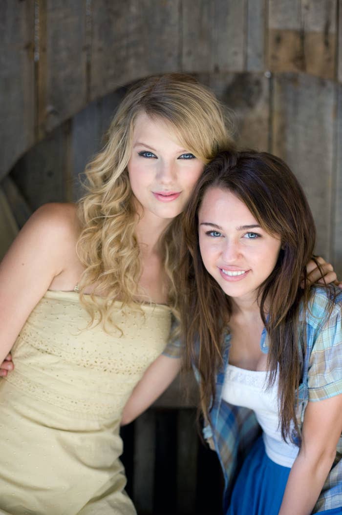 Taylor Swift and Miley Cyrus pose together, Taylor in a strapless dress and Miley in a plaid shirt and skirt