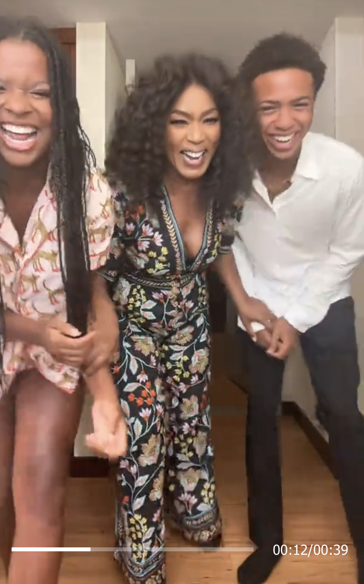 Angela Bassett, in a floral jumpsuit, laughs with two others; one wears a patterned dress, and the other a white shirt, in a candid moment. Timer at 0:12/00:39