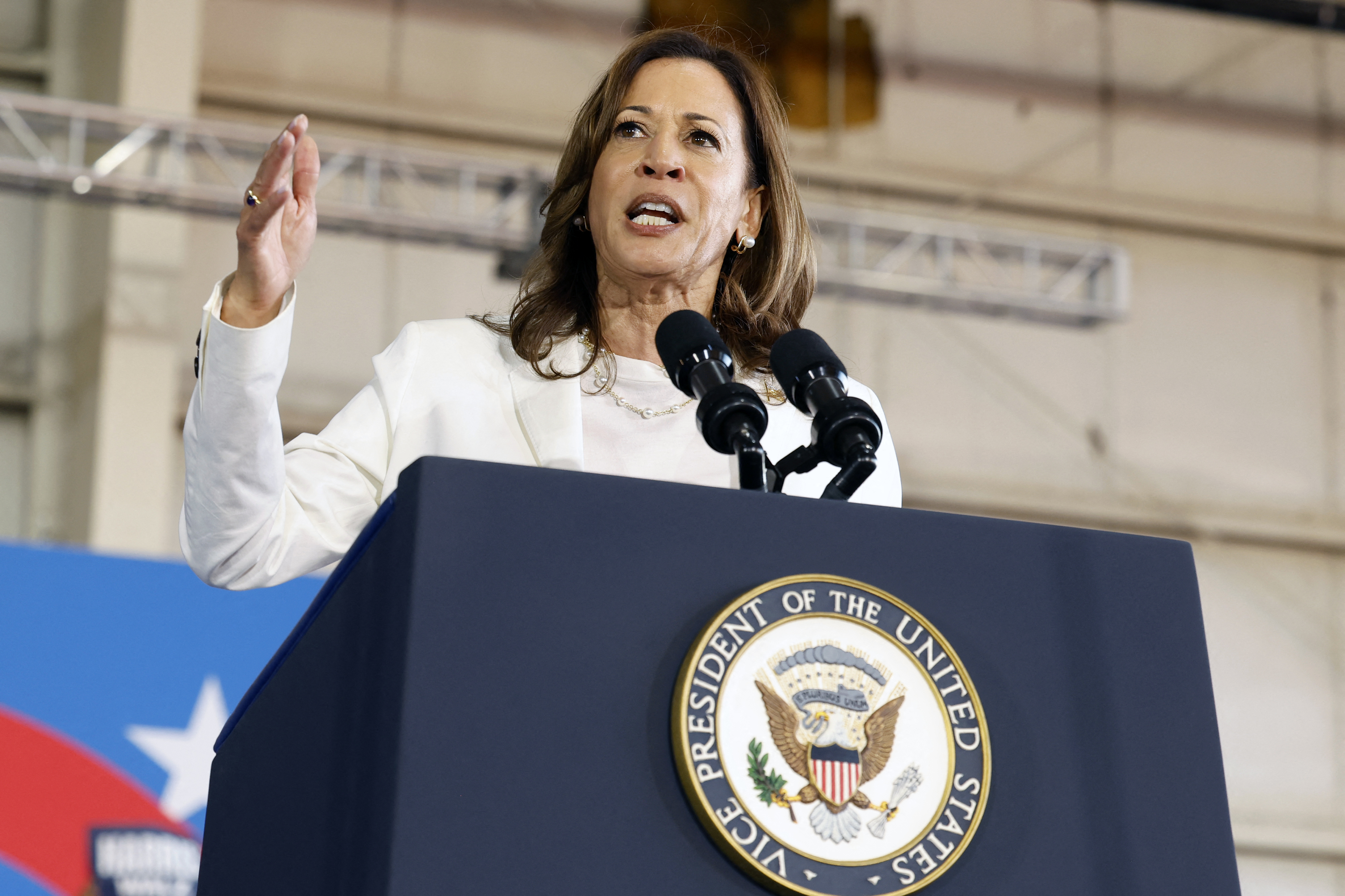 Kamala Harris speaks at a podium with the seal of the Vice President of the United States, addressing an audience in an indoor event space