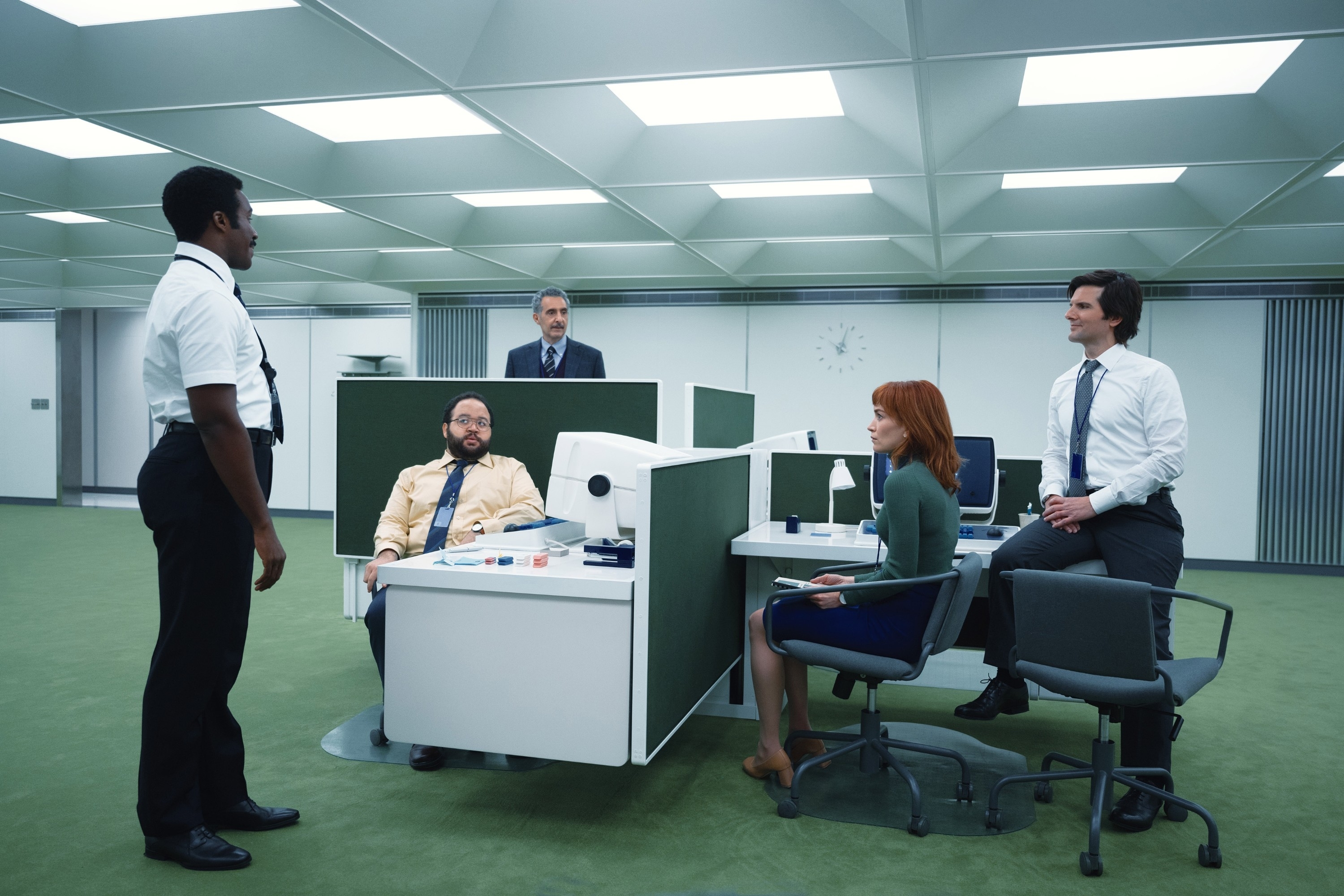Scene from &quot;Severance&quot; with five actors in an office: one standing, three seated, one leaning on a desk, with a modern, minimalist office setting