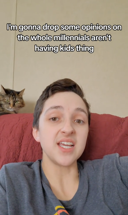 Person lying on a couch with a cat in the background. Text reads: "I'm gonna drop some opinions on the whole millennials aren't having kids thing."