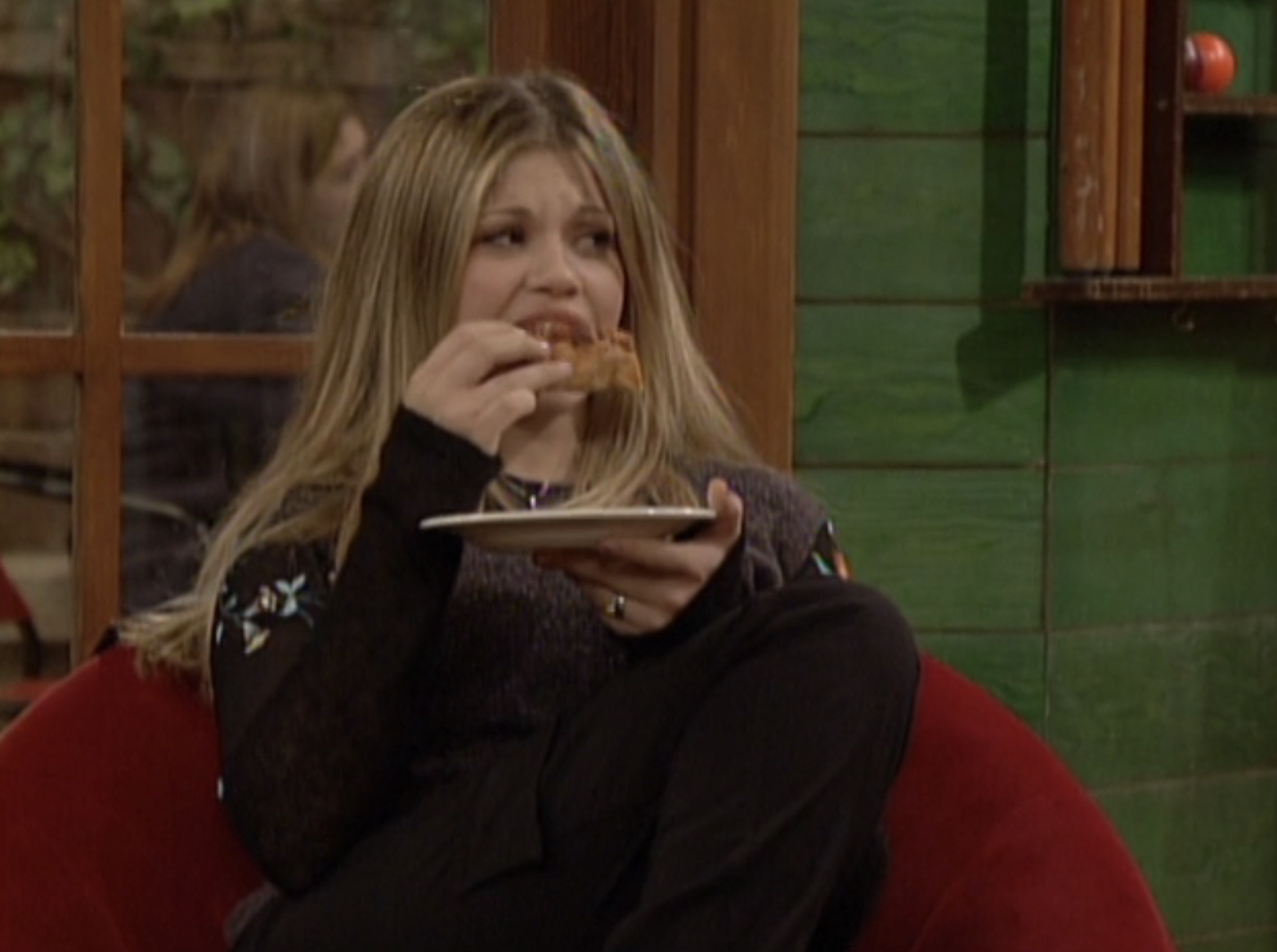 Danielle Fishel is shown sitting in a chair in a cozy room, eating with a plate in her hand