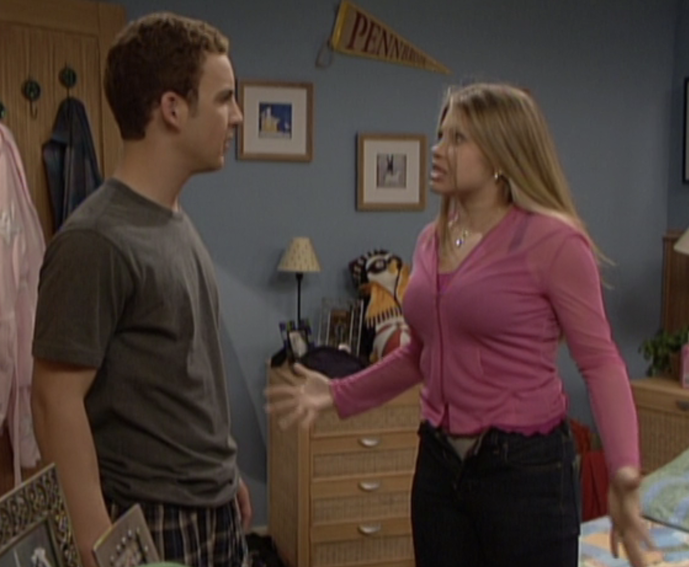 Two people, Cory Matthews and Topanga Lawrence, are talking in a bedroom. Cory wears a t-shirt and plaid shorts; Topanga wears a pink top and black pants