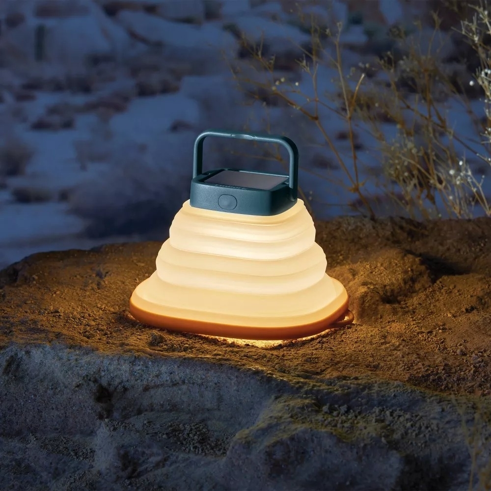 The illuminated camp lantern resting on a rock outside at night