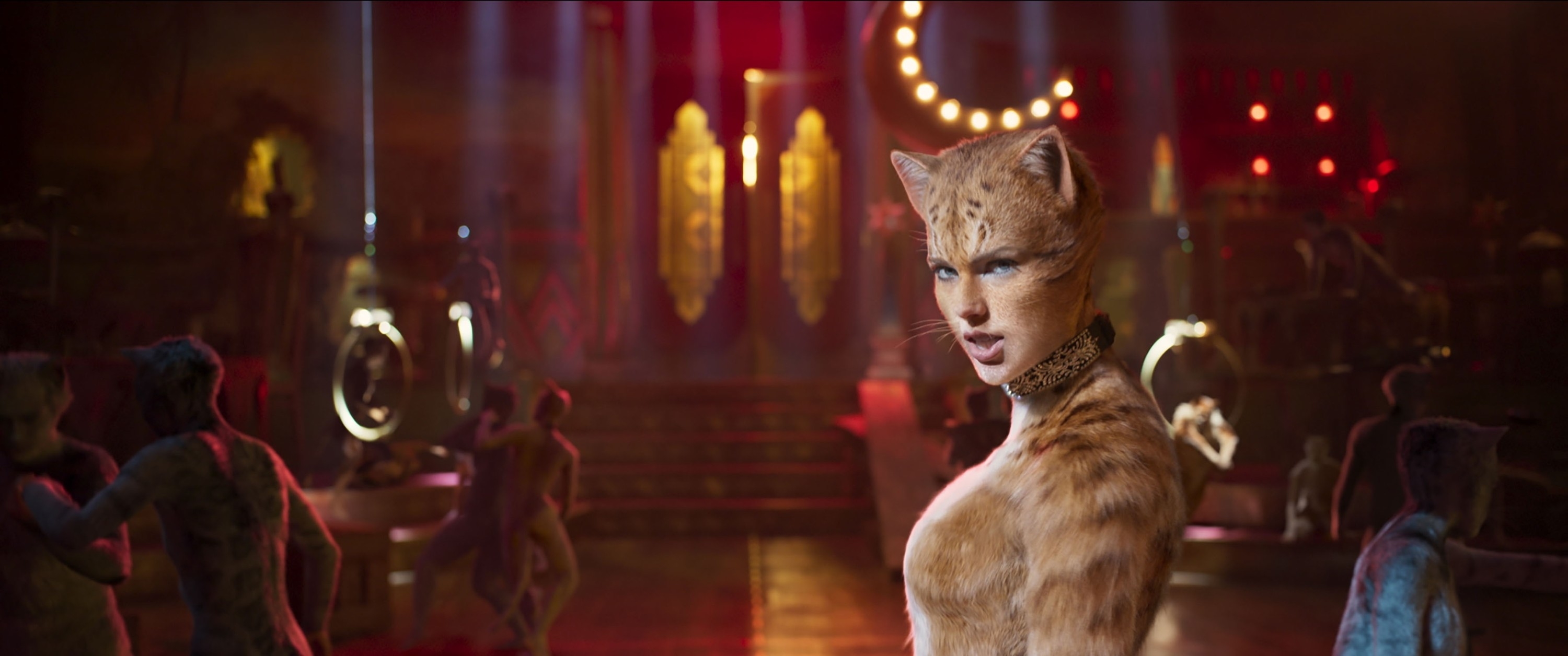 Taylor Swift in a cat costume with cat makeup stands on a stage with other cat-costumed characters in the background, likely from a scene in the movie &quot;Cats.&quot;