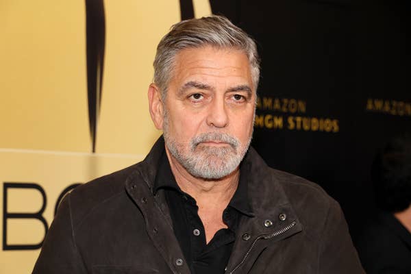 George Clooney, wearing a dark jacket over a black shirt, attends an event with an Amazon MGM Studios backdrop
