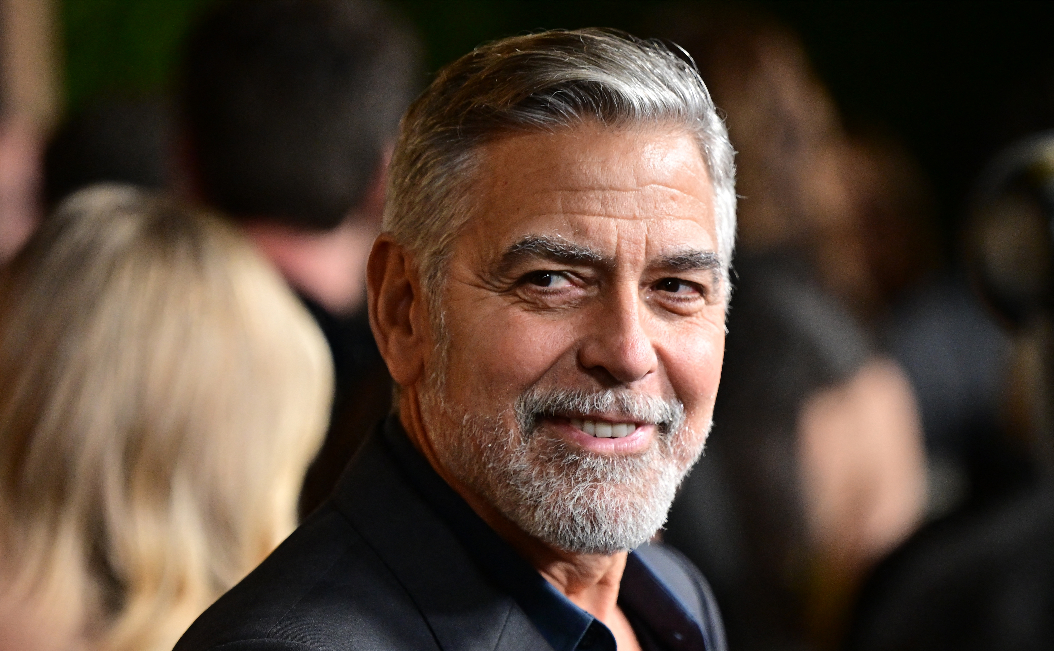 George Clooney, smiling and wearing a dark suit, at a public event