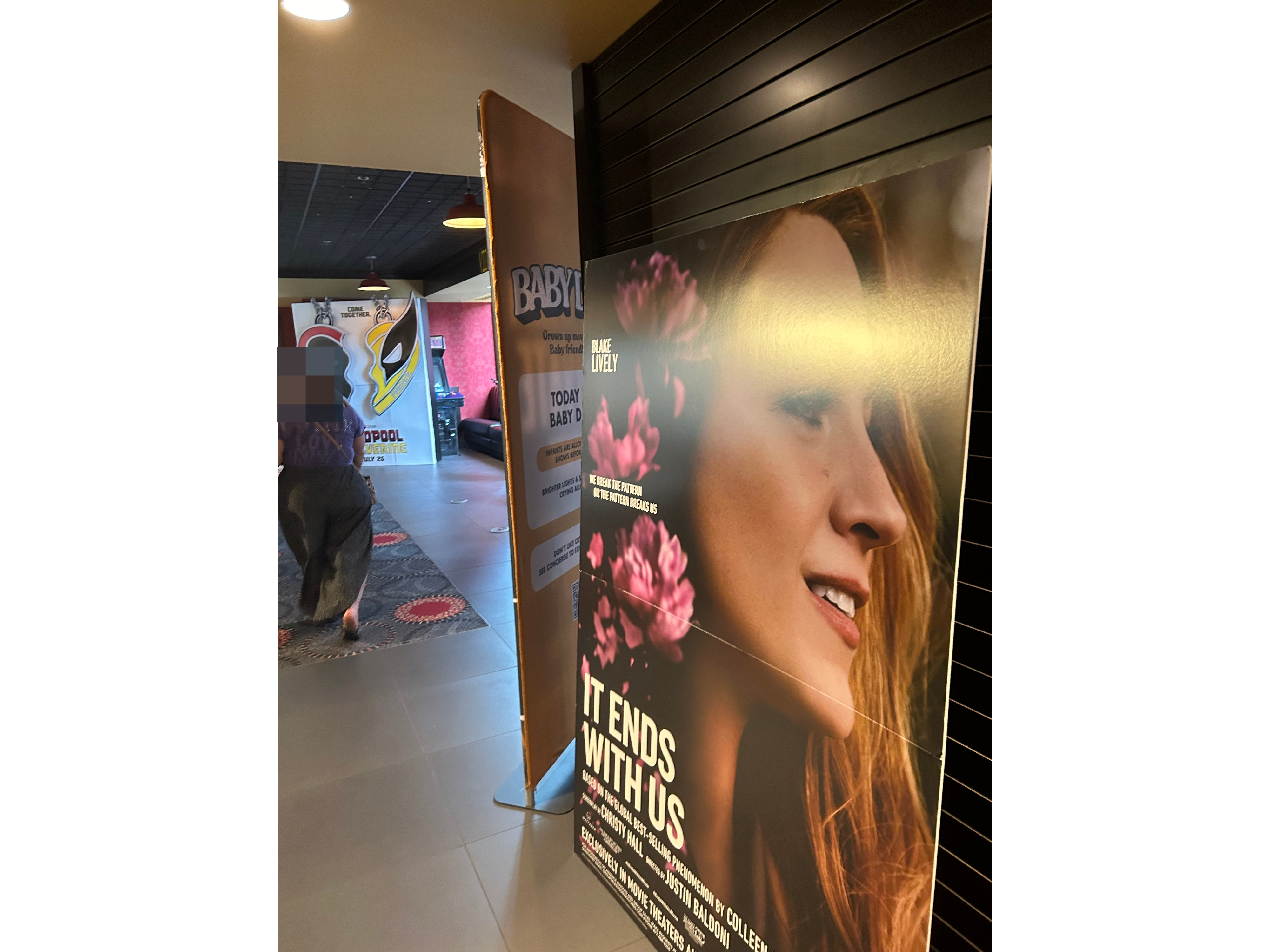 A movie poster in a theater lobby features Blake Lively for the film &quot;It Ends With Us.&quot; Nearby posters include advertisements for &quot;Baby.&quot;