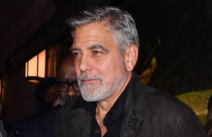 George Clooney, wearing a dark button-up shirt and jacket, stands outdoors at an evening event
