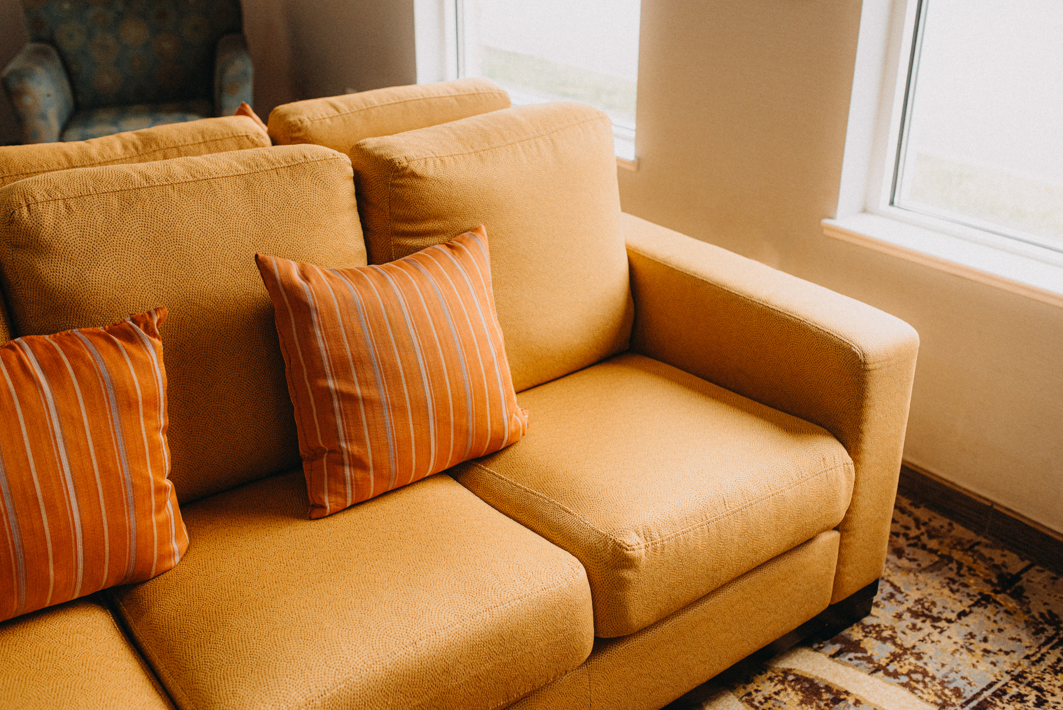 A cozy, modern living room with a tan sofa and orange-striped pillows, positioned near large windows