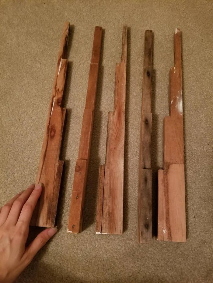 Five thin pieces of wood with stepped edges are laid out on the floor. A hand is touching the leftmost piece
