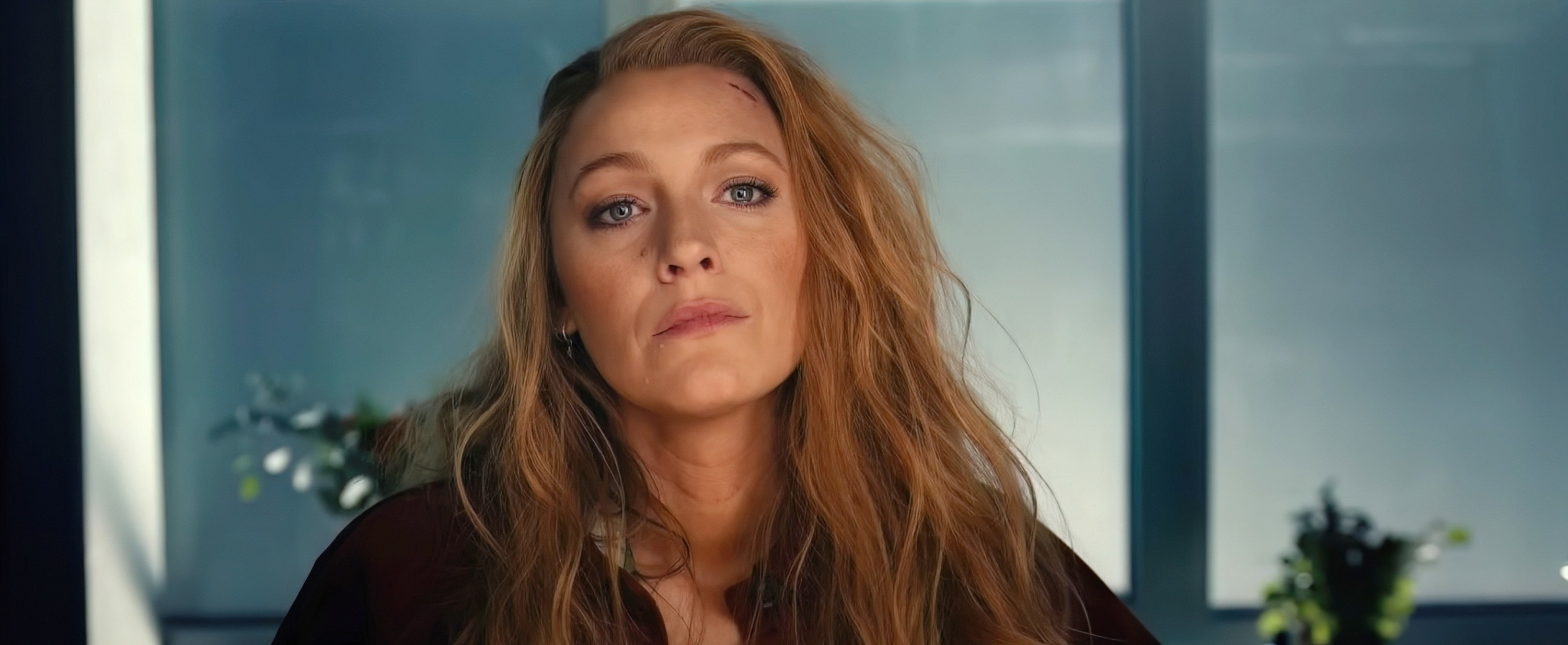 Blake Lively with tousled hair and a visible wound on her forehead, looking at the camera with a neutral expression in an indoor setting