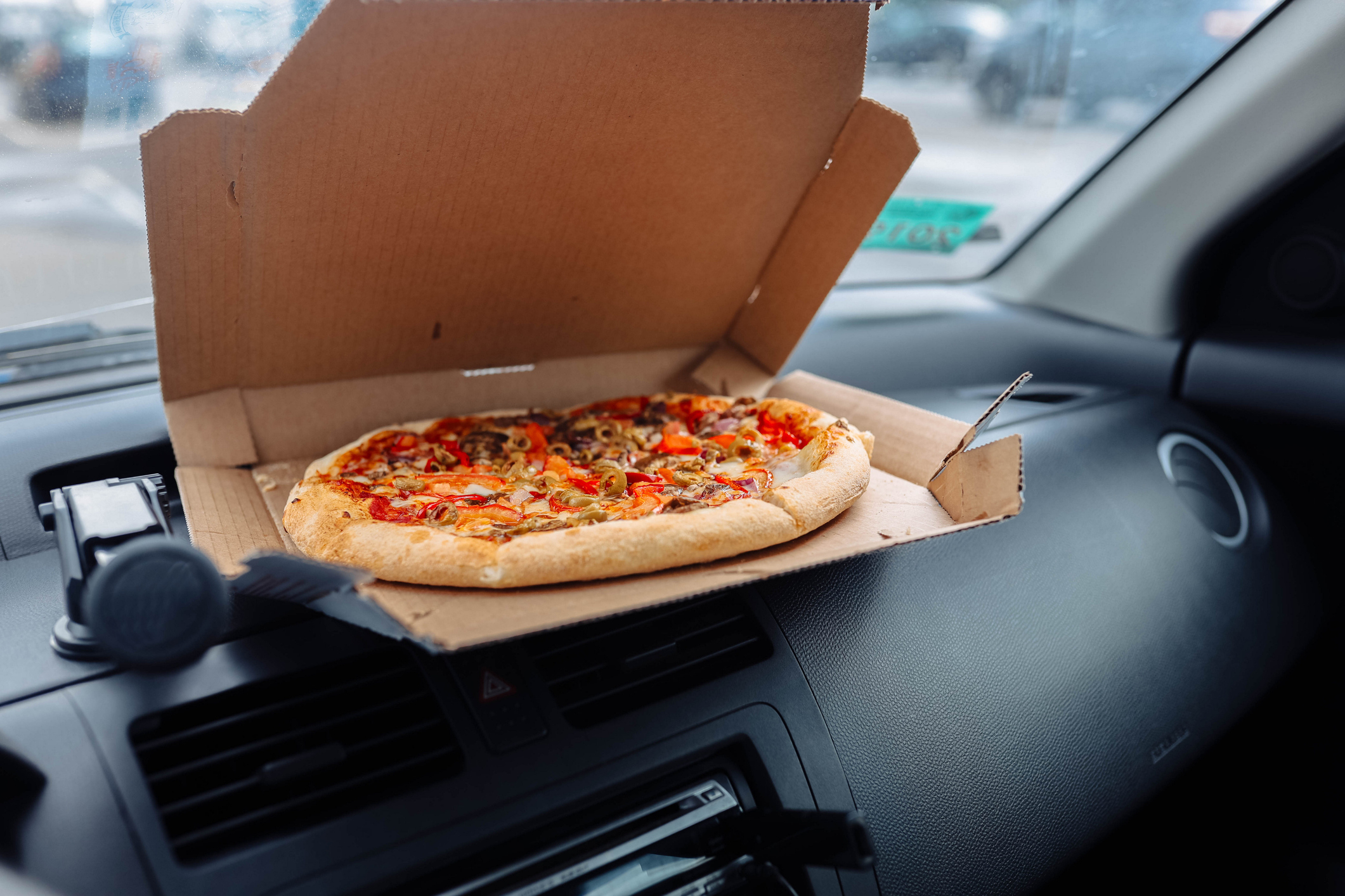 A pizza box with a pizza inside is placed on the dashboard of a car