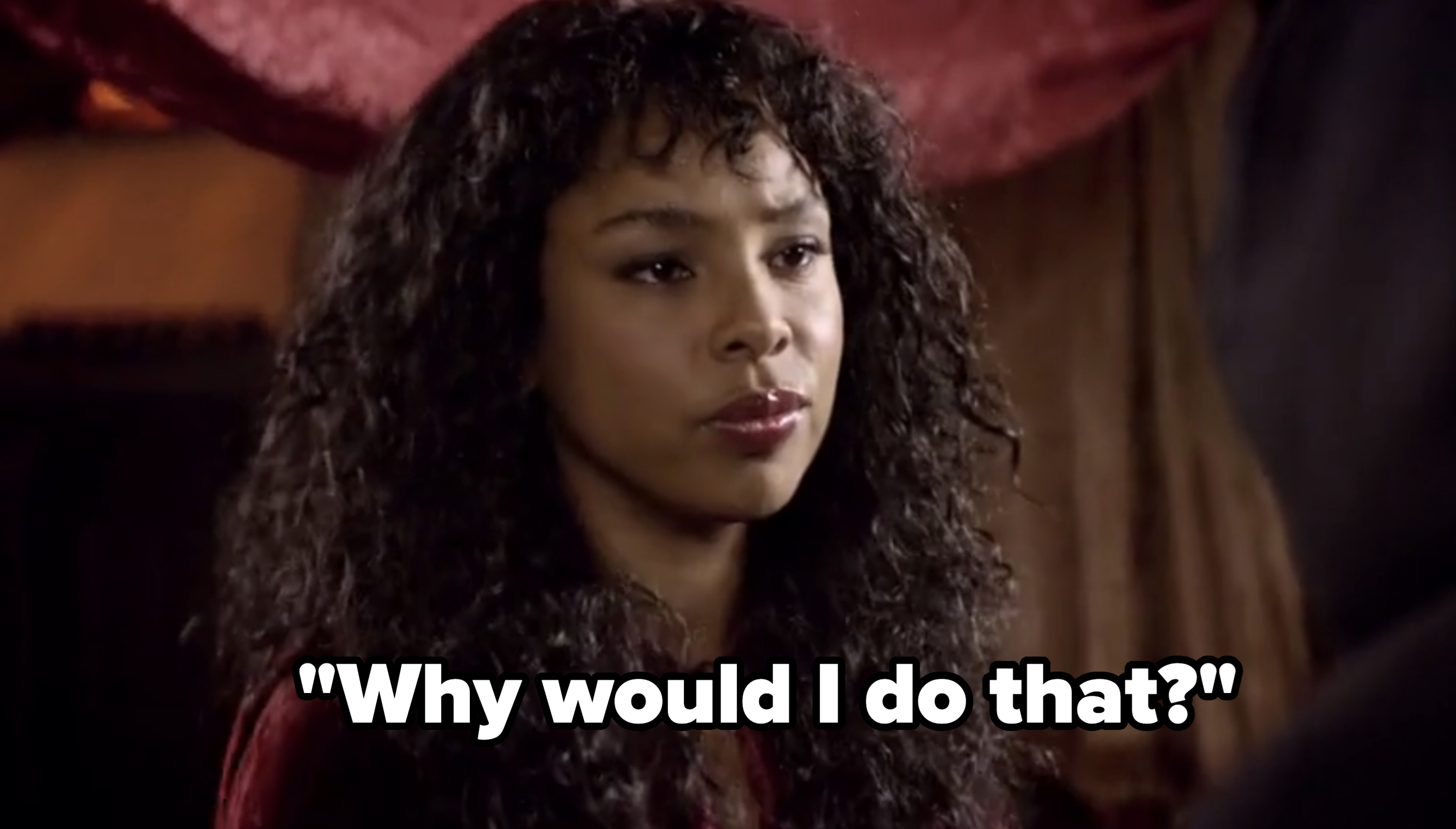 A person with long, curly hair gazes intently at someone off-image. The background is softly blurred