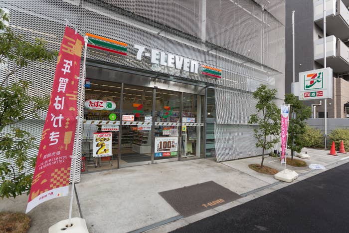 Exterior of a 7-Eleven store with promotional banners and a clear view of the entrance, displaying store signage and promoting product offers