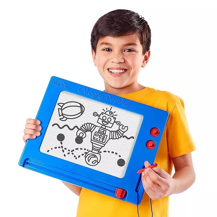 A young child holds a Magna Doodle featuring a drawing of a robot and a blimp