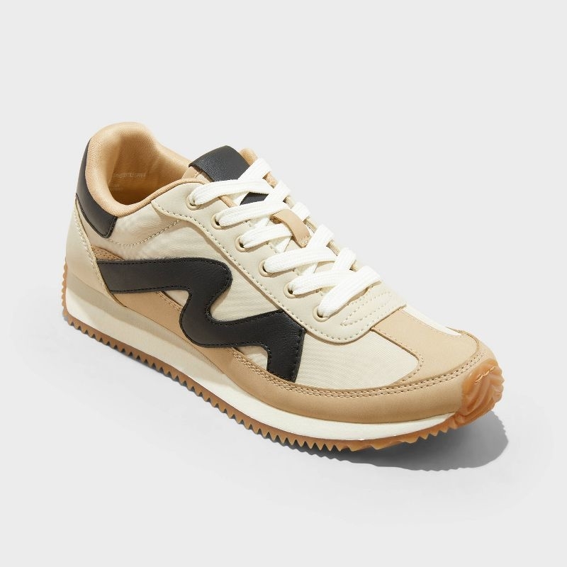 Athletic sneaker with a beige and black wave design, white laces, and a ridged sole, displayed for a shopping article