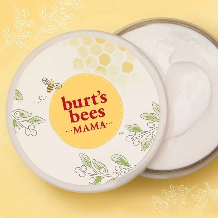 Burt's Bees Mama cream in an open container with a lid featuring a bee and floral design on a yellow background