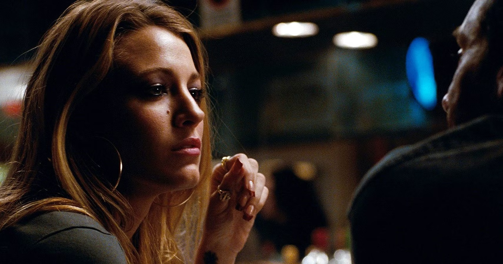 Blake Lively está en un bar sentada, mirada pensativa, con grandes pendientes de aro