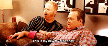 Jesse Tyler Ferguson and Eric Stonestreet sitting on a couch watching TV. Text: &quot;This is my new favorite show.&quot;