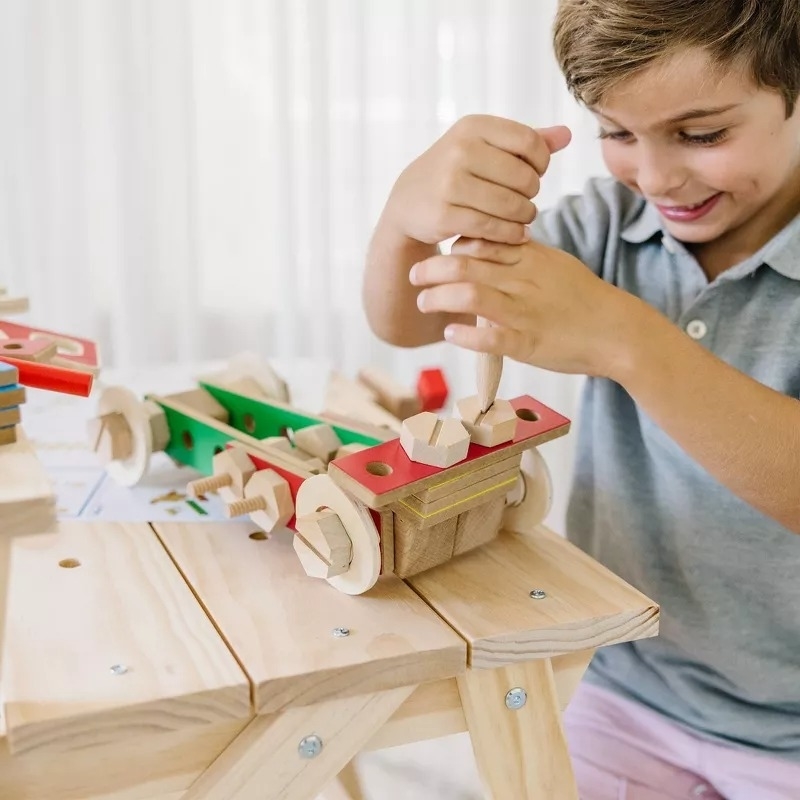 A young child is happily assembling a wooden toy car set at a table