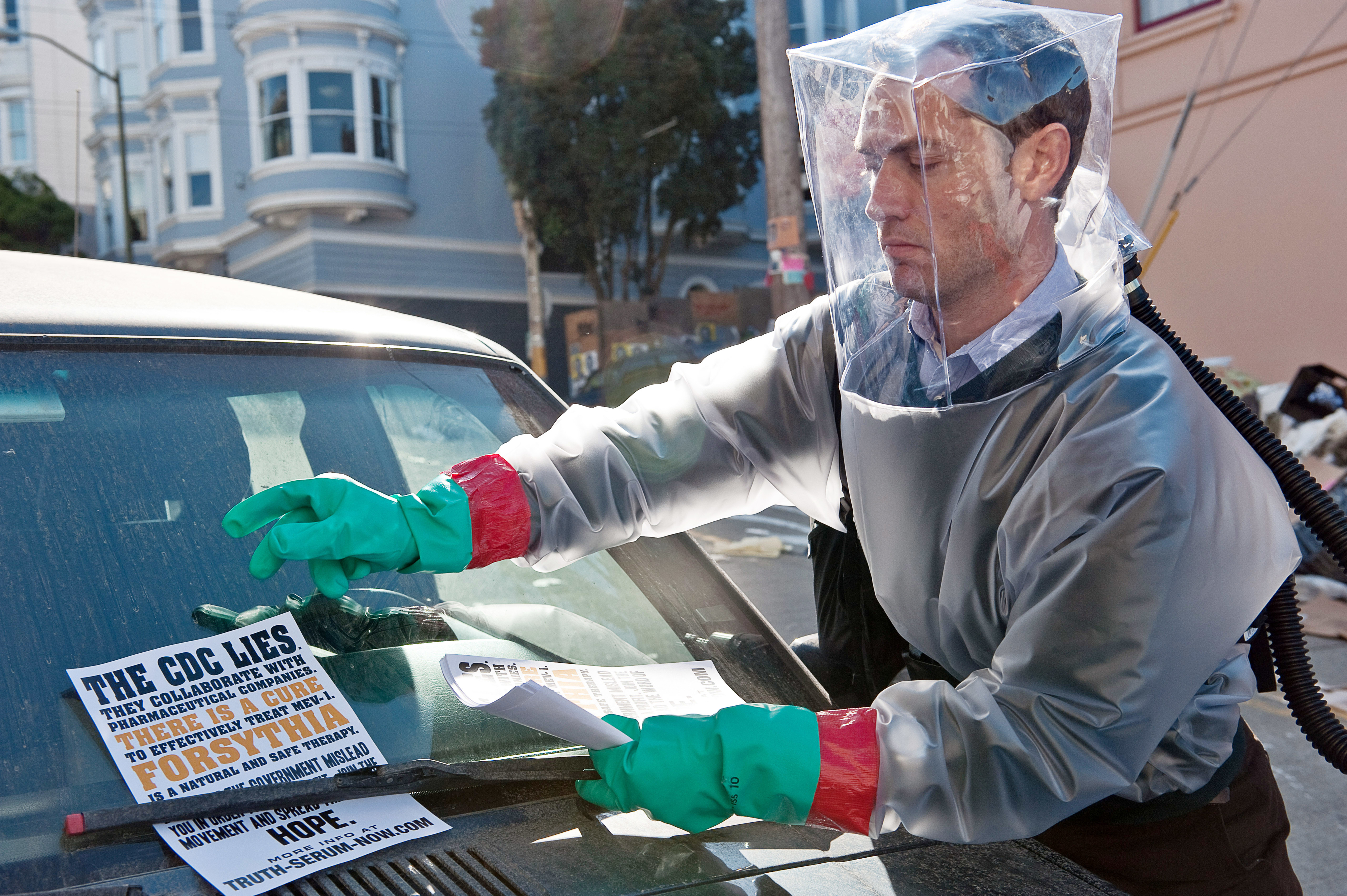 Jude Law in protective gear as he puts flyers on a car in &quot;Contagion&quot;