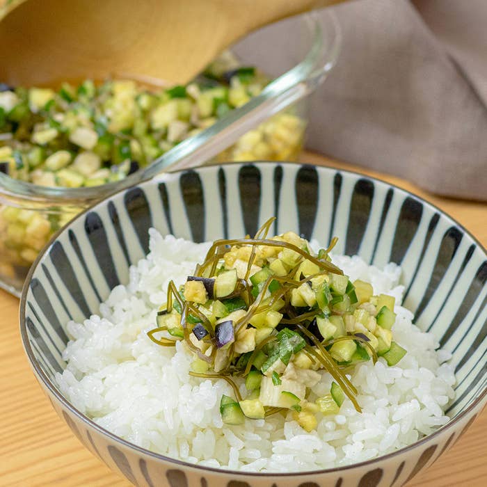 ボウルに盛られたご飯の上に、細かく刻まれた野菜と昆布がのっている。背景に予備の具材が入った容器。
