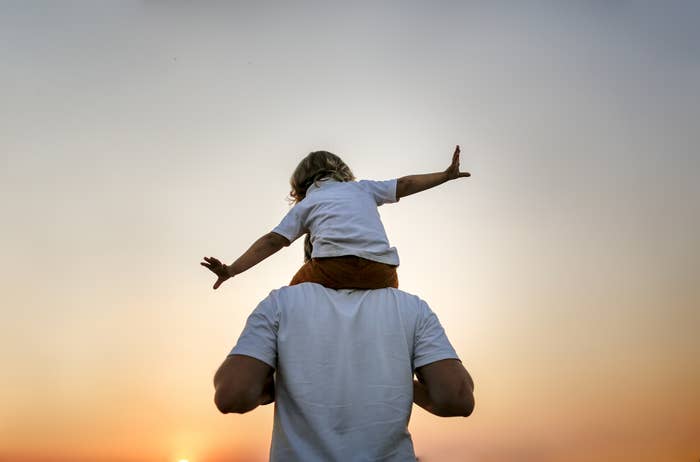 Person with a kid on their shoulders with a sunset scene in the background