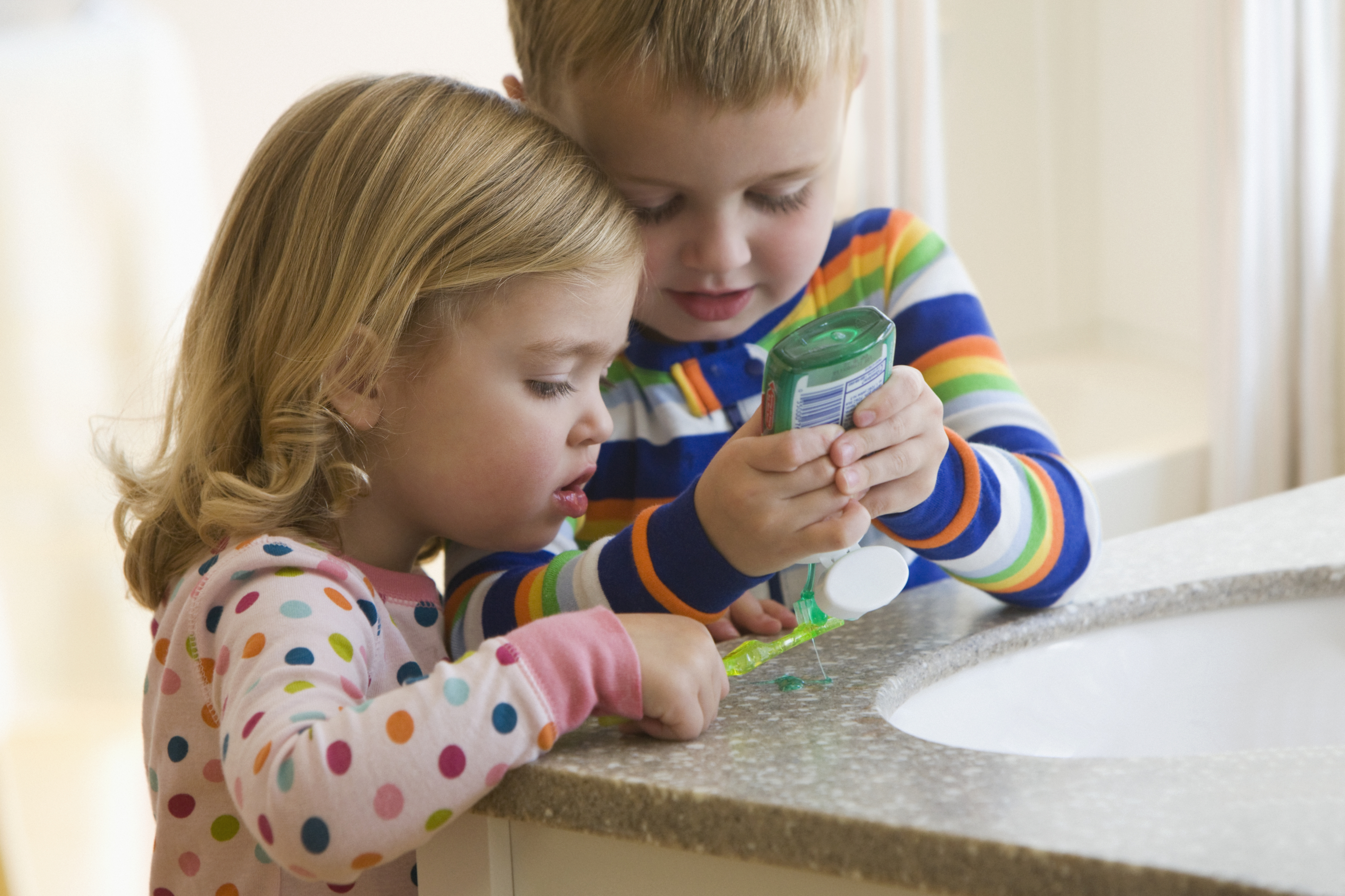 Two kids squeezing toothpaste on a bathroom counter