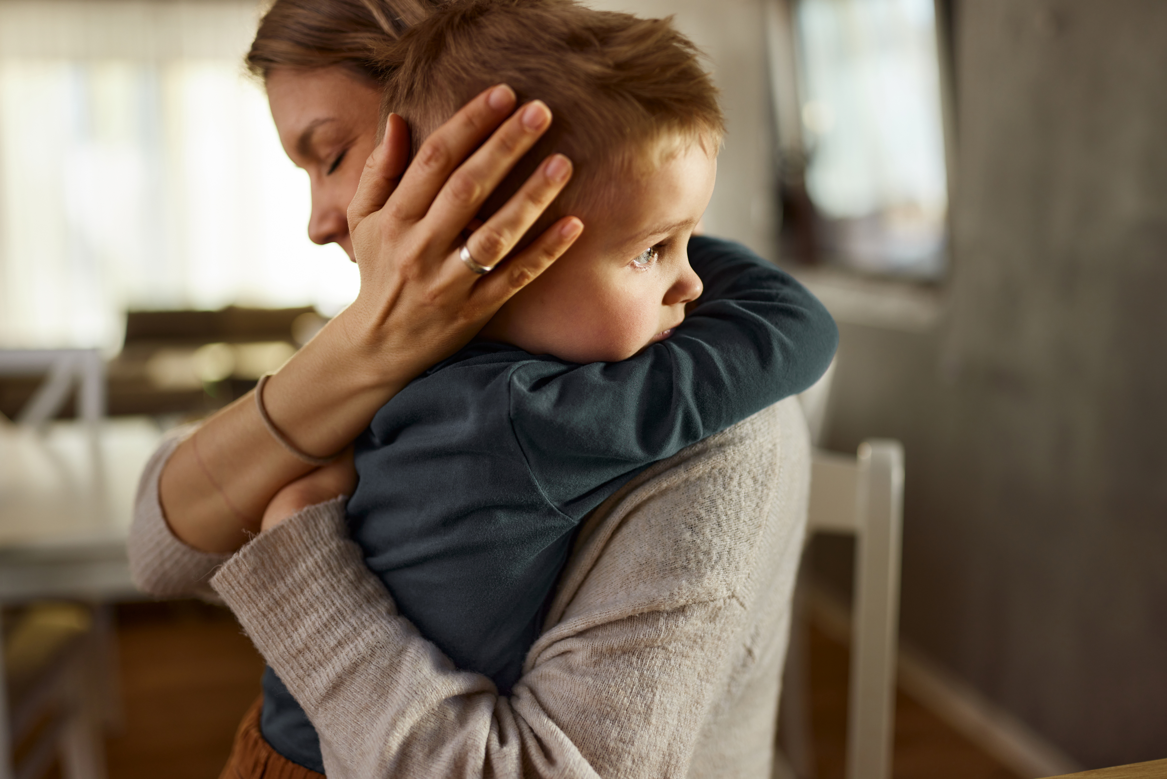 A woman gently hugs a young boy, who rests his head on her shoulder