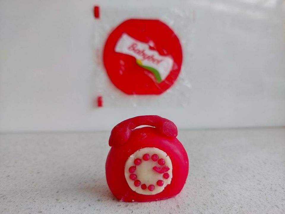 Round, red candy shaped like a rotary phone with dial details, in front of a partially opened Ricola candy wrapper