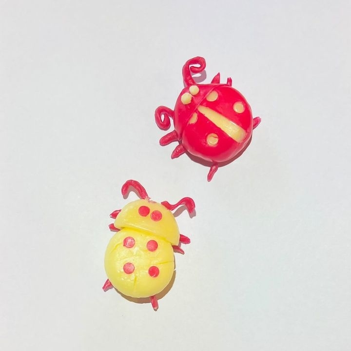 Two cheese wheels crafted as ladybugs, one in yellow and one in red, with detailed antennae and spots
