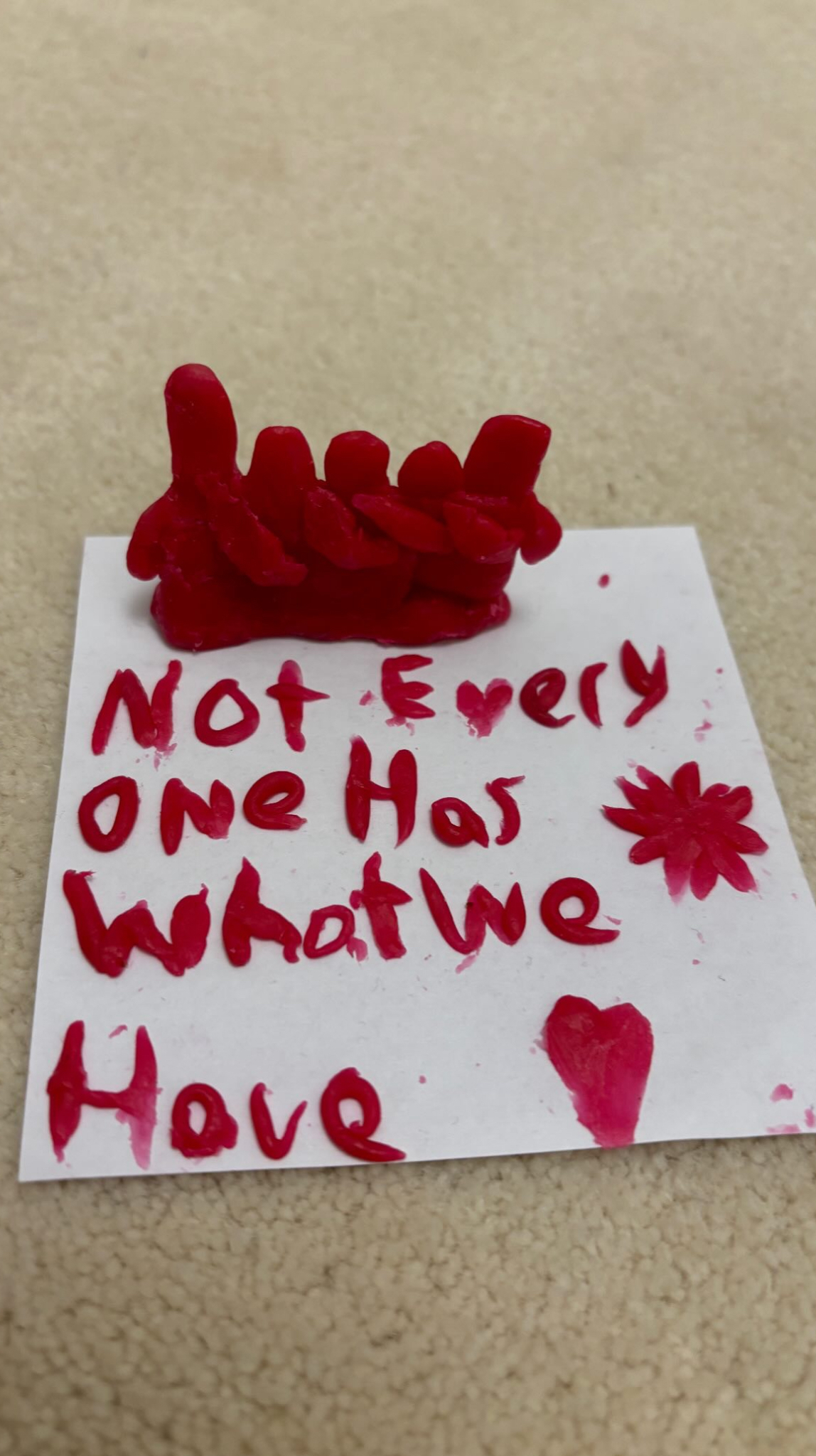 Small red clay sculpture with handwritten text on a paper says: &quot;Not Everyone Has What We Have&quot; with a heart and a star drawing
