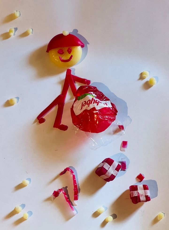 A stick figure made from candy wrappers and cheese wax holds a small ball labeled &quot;Babybel.&quot;
