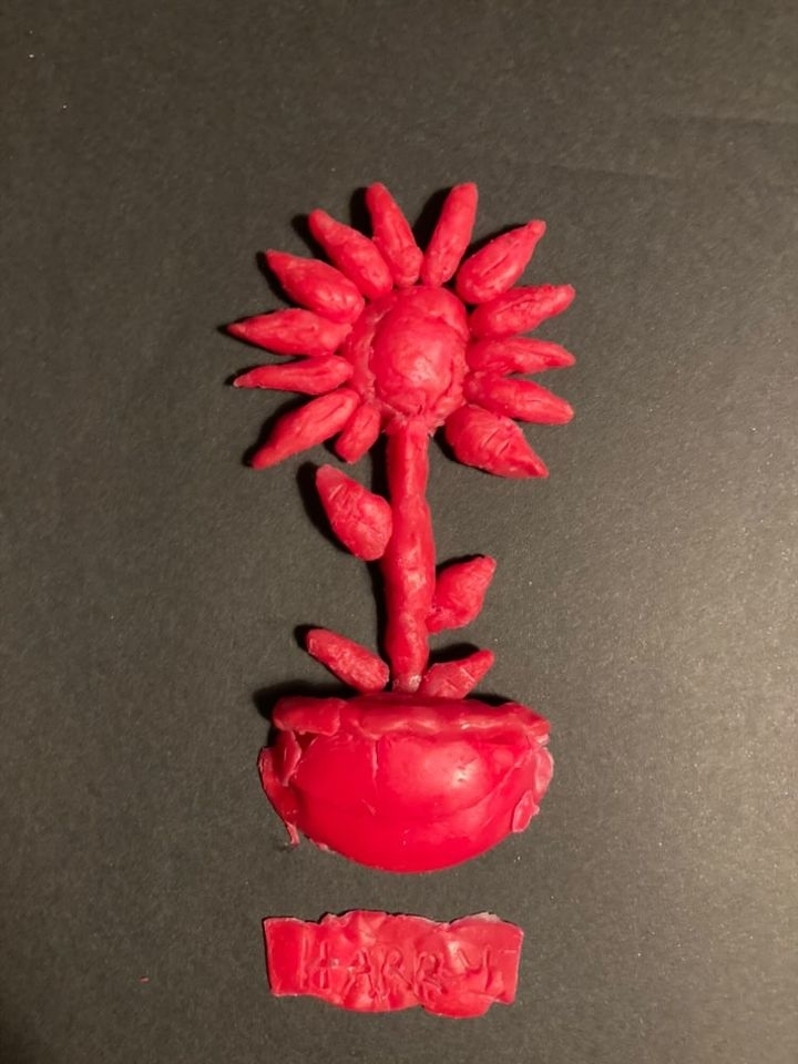 A handcrafted clay model of a sunflower with a potted base and small rectangular plaque