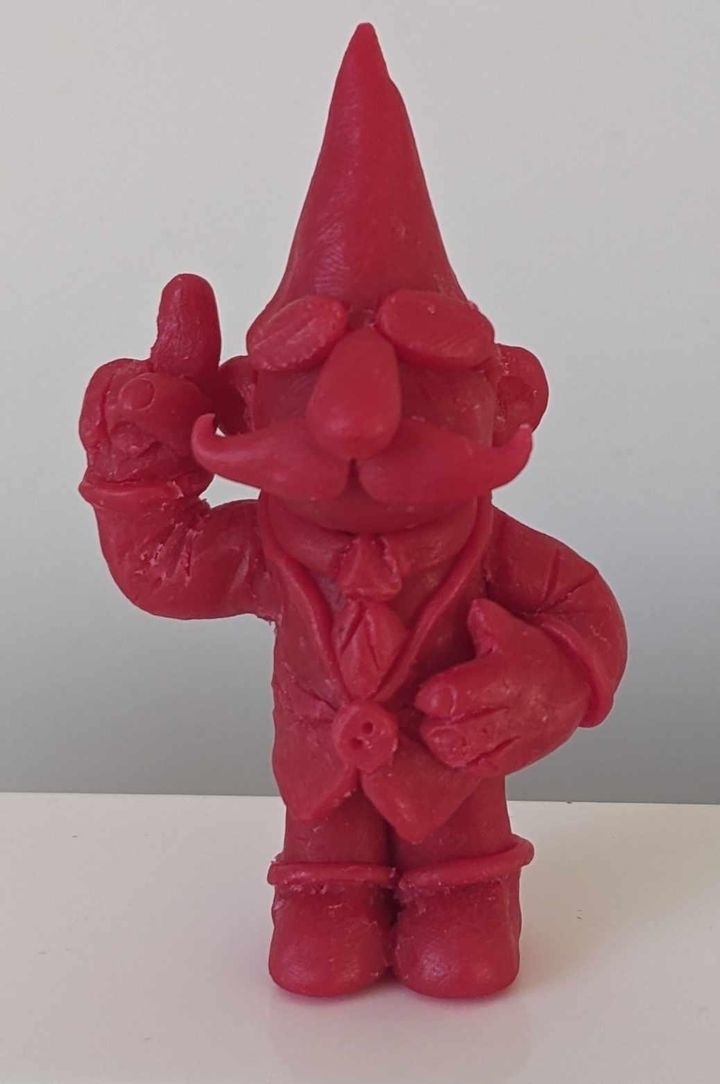 A red garden gnome wearing a suit and tie, with a pointed hat and a mustache, raising its right index finger