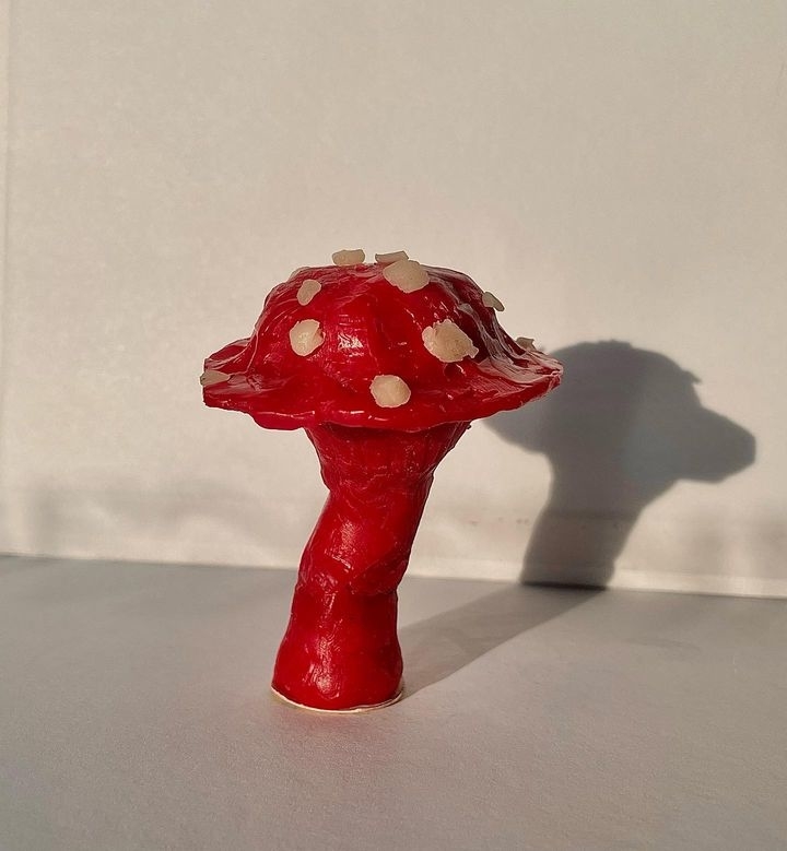 A red mushroom sculpture with white spots, standing against a plain background