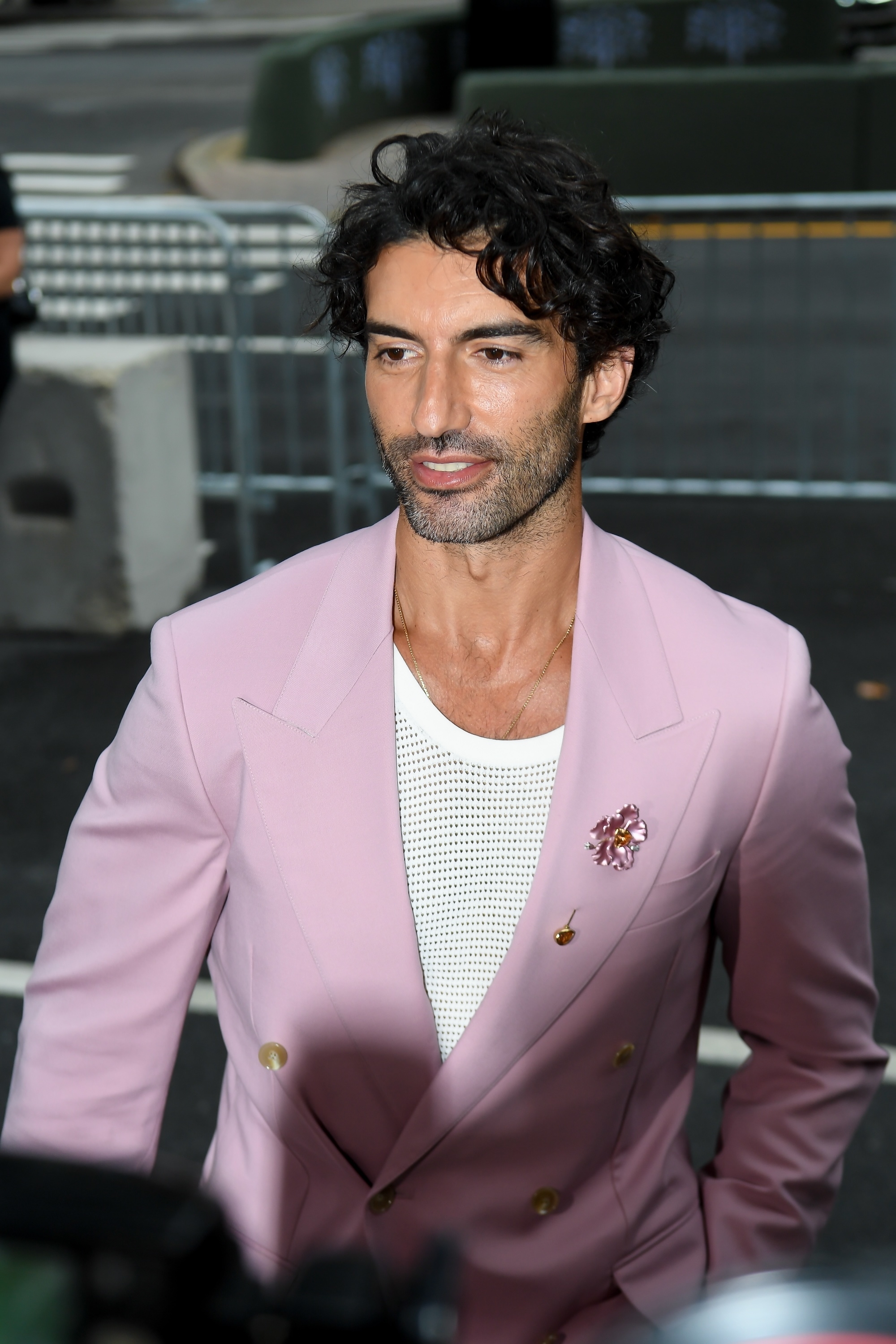 Justin Baldoni in a stylish pastel blazer with a mesh shirt, outdoors during a public event