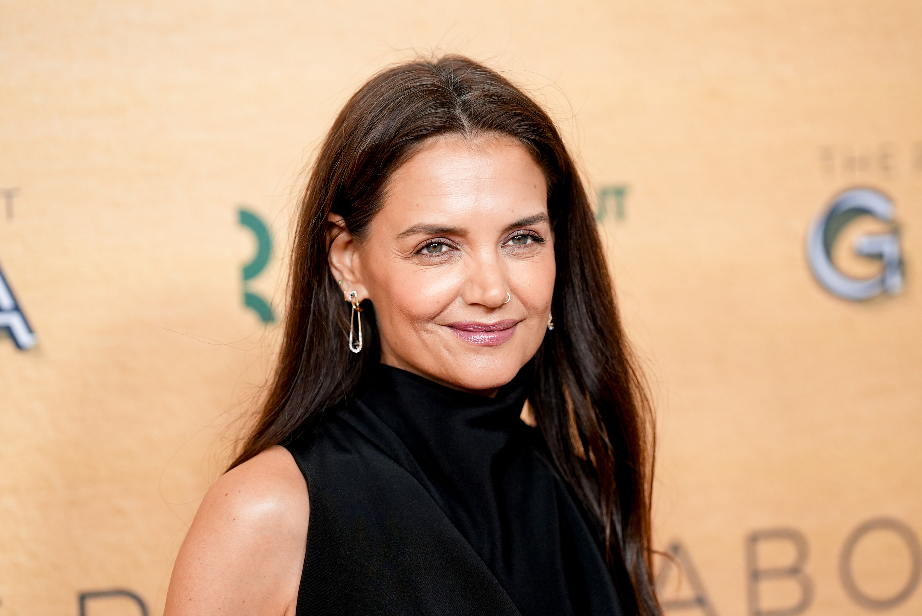 Katie Holmes, wearing a sleek black dress, smiles while posing at a formal event