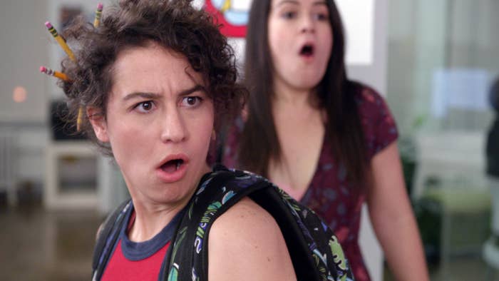 Ilana Glazer and Abbi Jacobson appear surprised, with Ilana having pencils in their hair and wearing casual attire
