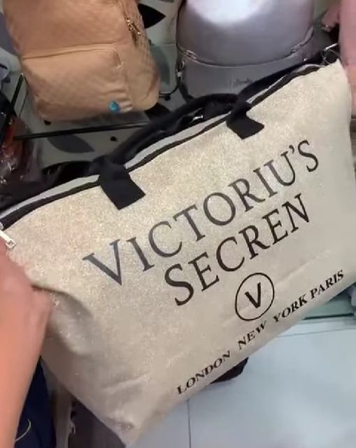 A close-up of a large white bag with black handles, featuring the text "VICCTORIU'S SECRET LONDON NEW YORK PARIS" on it