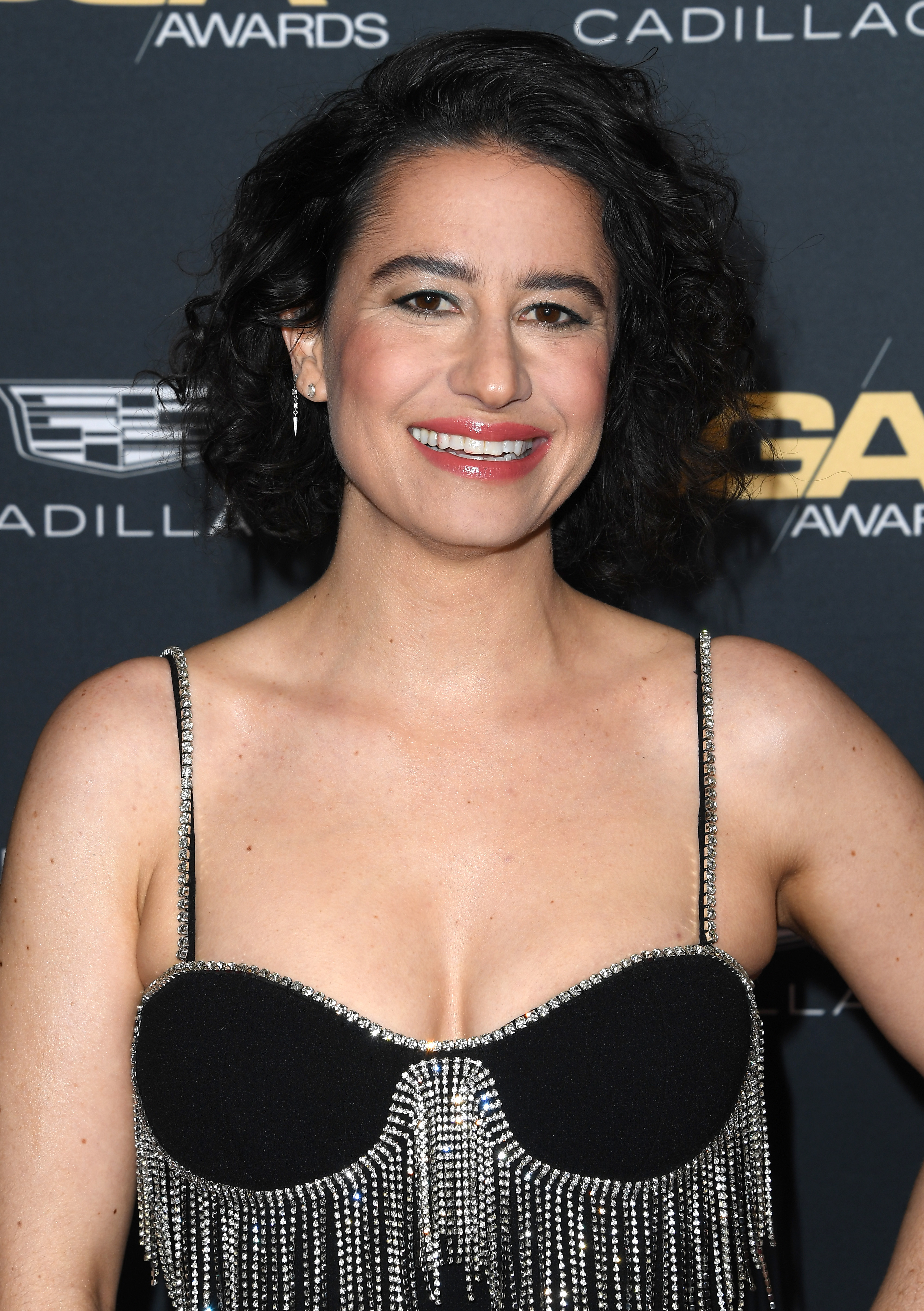 Ilana Glazer smiles on the red carpet, wearing a sparkling, beaded dress with spaghetti straps at an awards event