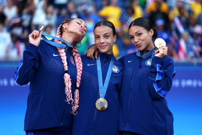 Three athletes wear tracksuits and proudly show off their medals at an award ceremony