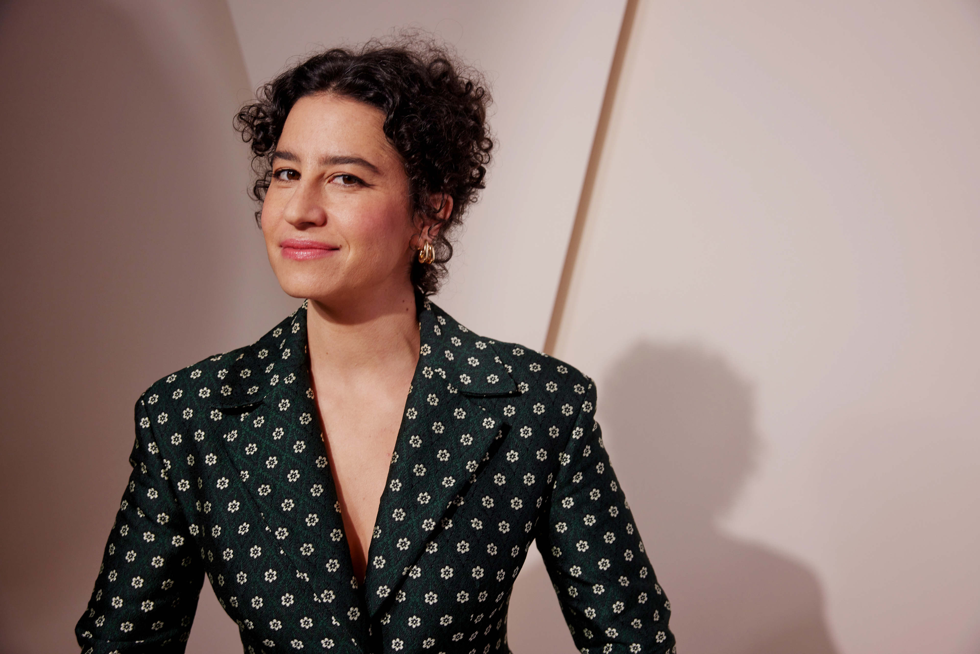 Ilana Glazer in a patterned suit jacket, posing with a slight smile at what appears to be a formal event