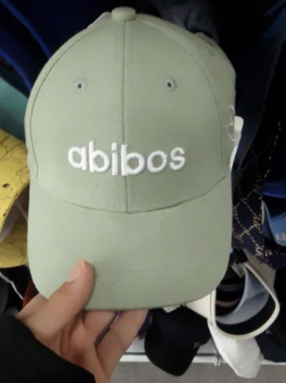 A hand holds a green baseball cap with the text "abibos" embroidered on the front
