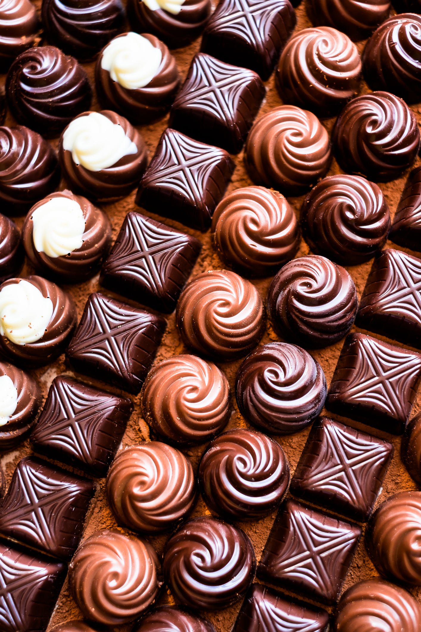 Rows of assorted chocolates, including swirled, patterned, and square designs