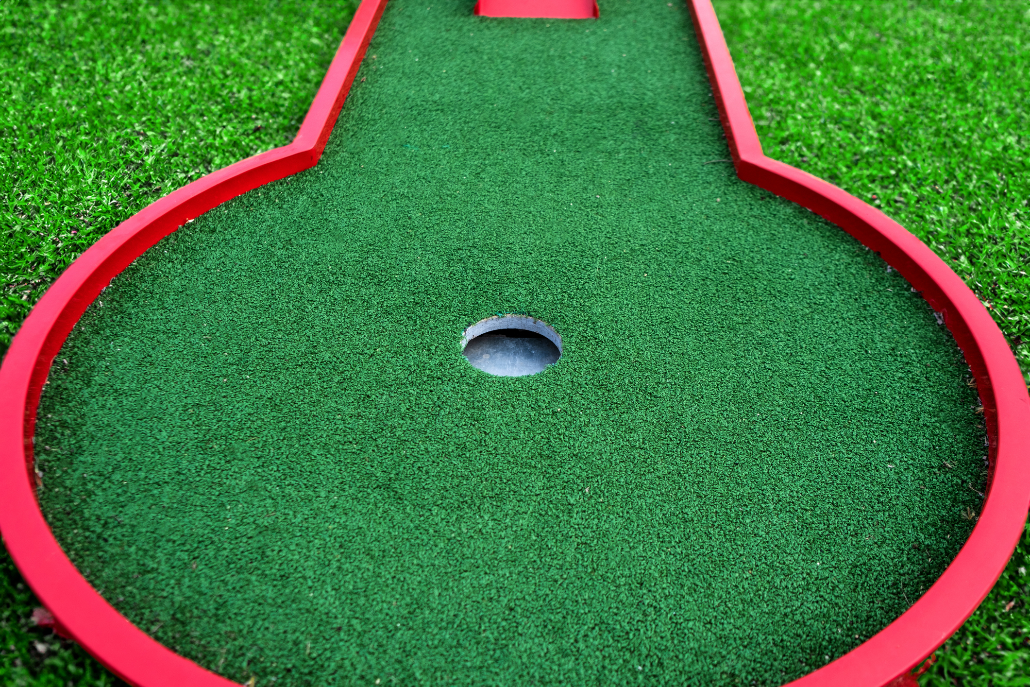 Close-up of a mini-golf hole with a green artificial turf and a red border
