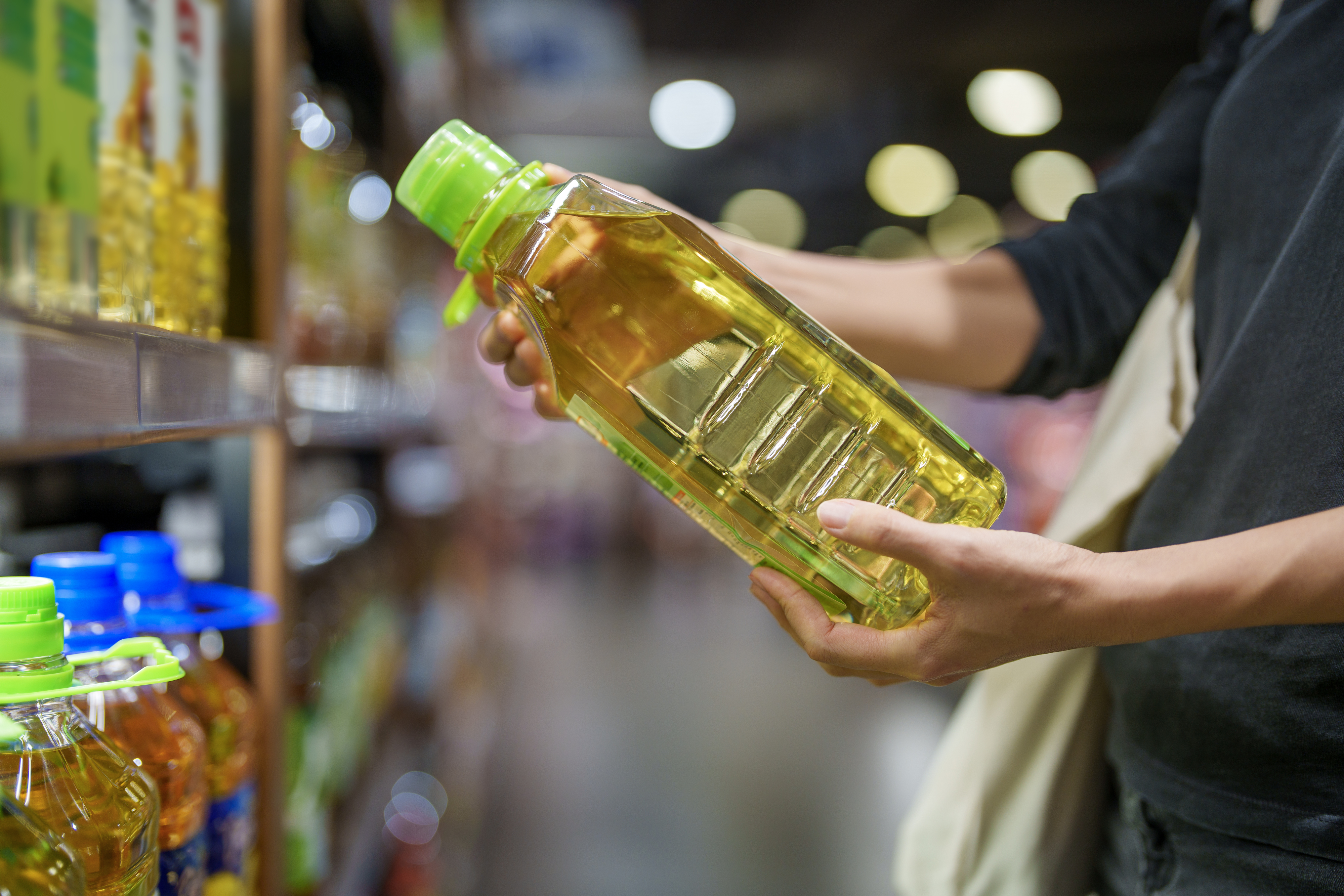 A person holds a bottle of cooking oil while grocery shopping in a well-lit supermarket