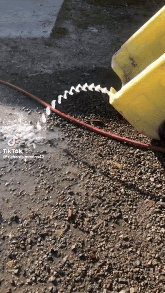Water pouring from a yellow container onto gravel, forming a spiral stream. TikTok username @richardsimmons42 is on the bottom of the image