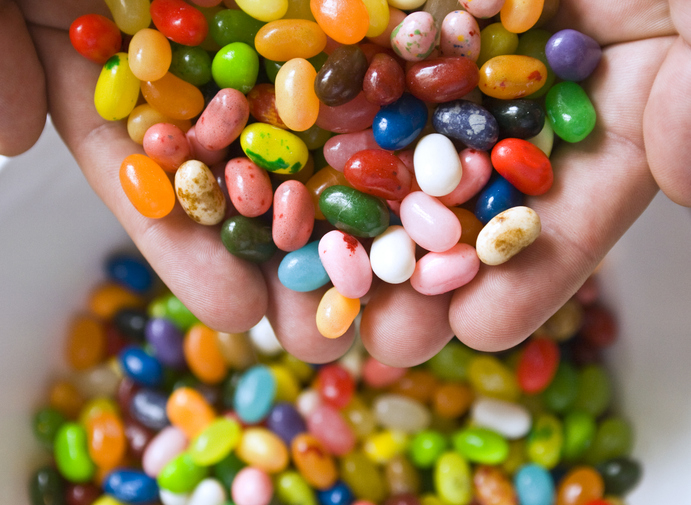 Two hands holding a variety of colorful jelly beans above a bowl filled with more jelly beans